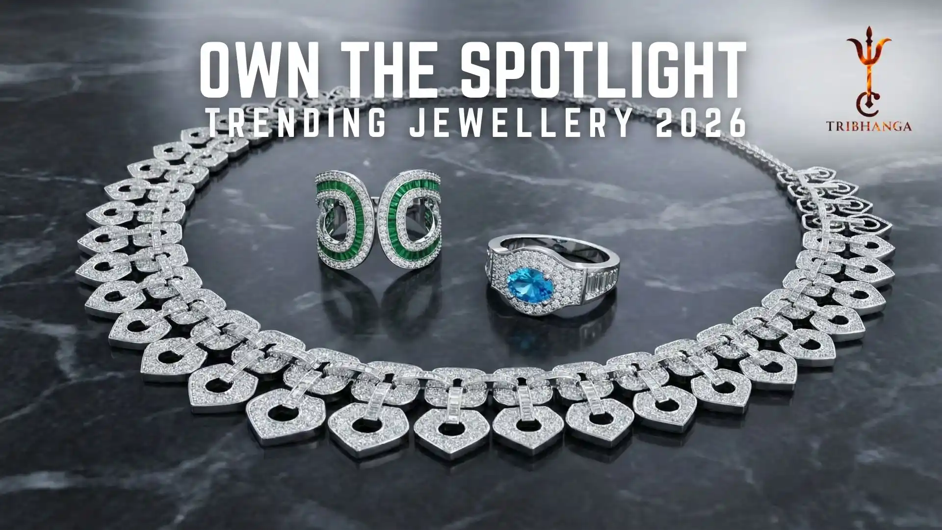 Diamond necklace and statement rings featuring emerald and blue gemstones on a dark marble background. Text reads: Own The Spotlight - Trending Jewellery 2026 by Tribhanga.